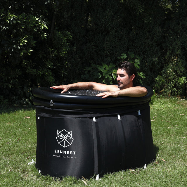 Man relaxing in the Zennest Oval 150 cold plunge tub filled with ice, on a garden lawn